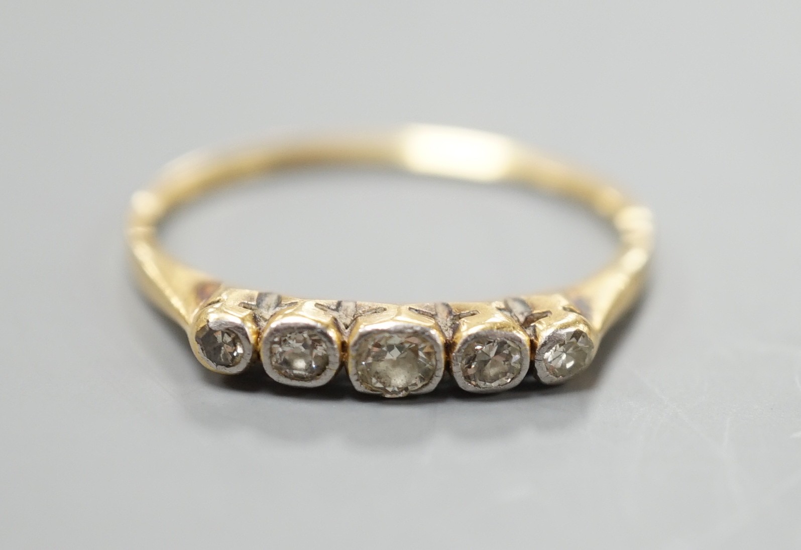 A yellow metal and graduated collet set five stone diamond half hoop ring, size O, gross weight 1.7 grams.